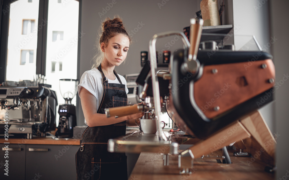 Portrait of professional barista woman in apron making coffee using machine at cafe