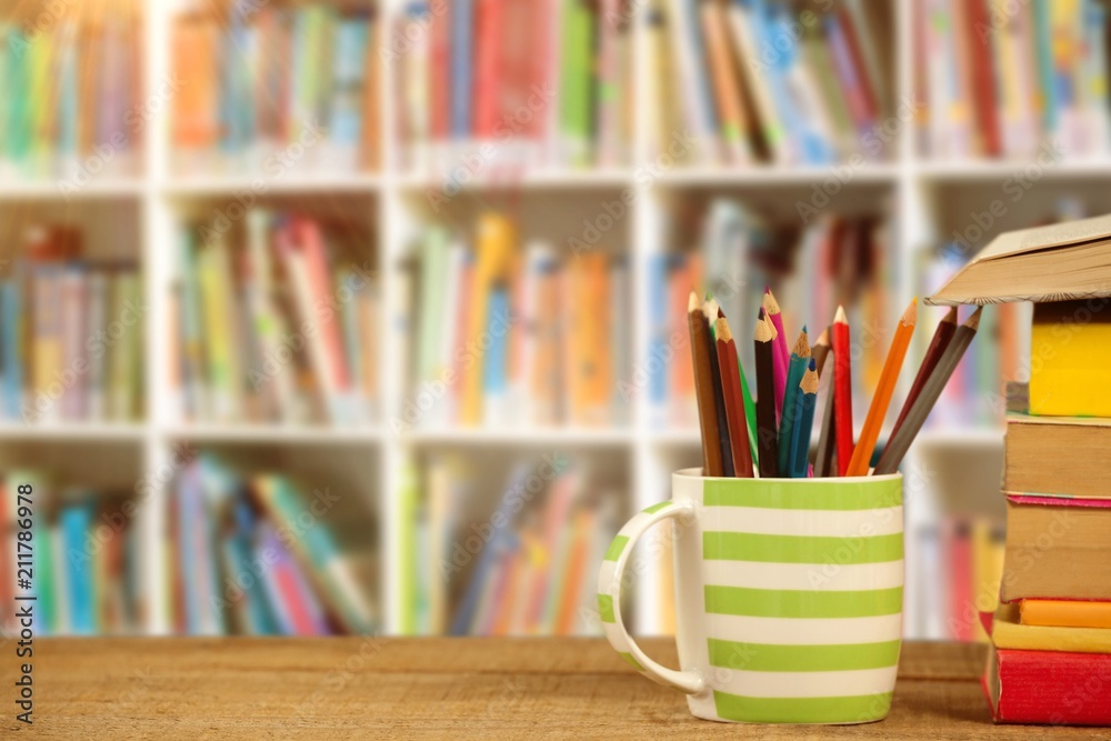 Composite image of stack of books by mug with colored pencils on