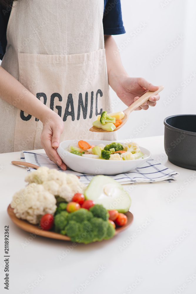 厨房里的女人在锅里烹饪蔬菜并品尝。