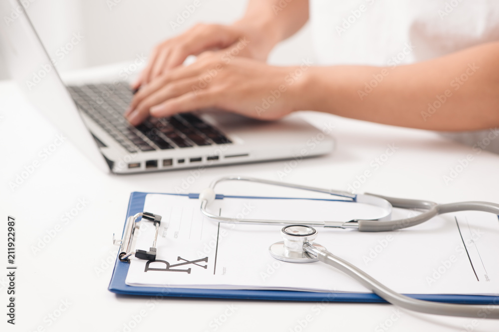 Close-up of a female doctor typing on laptop computer, sitting at the table in the hospital