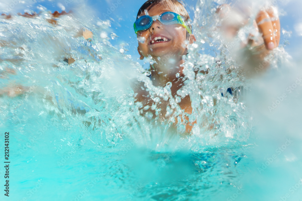 Happy boy having fun splashing water in the pool