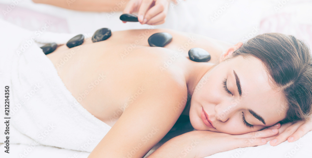 Hot stone massage treatment by therapist in spa.