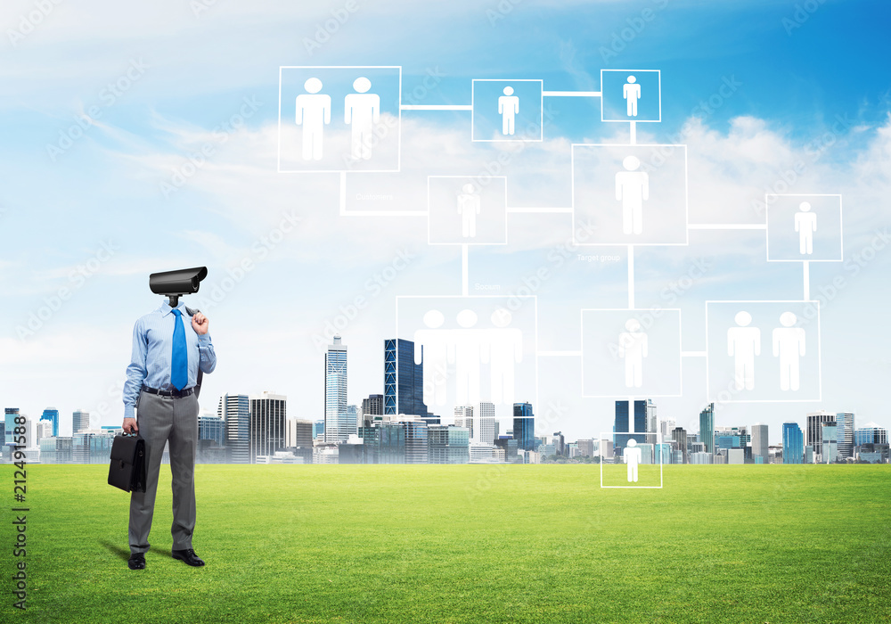 Camera headed man standing on green grass against modern cityscape