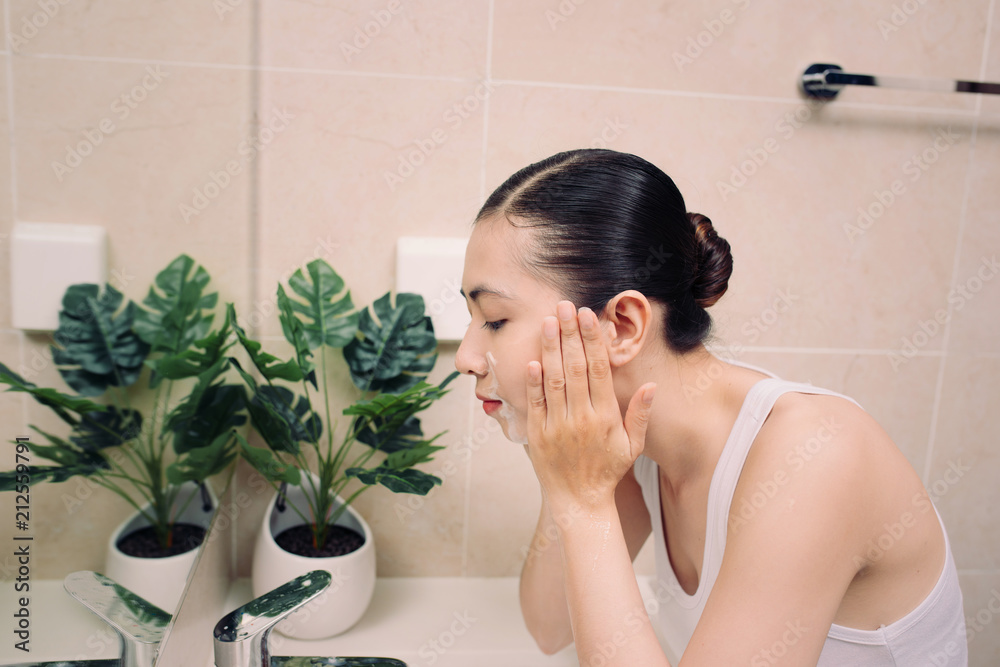 Woman happy cleanses the skin with foam in bathroom.