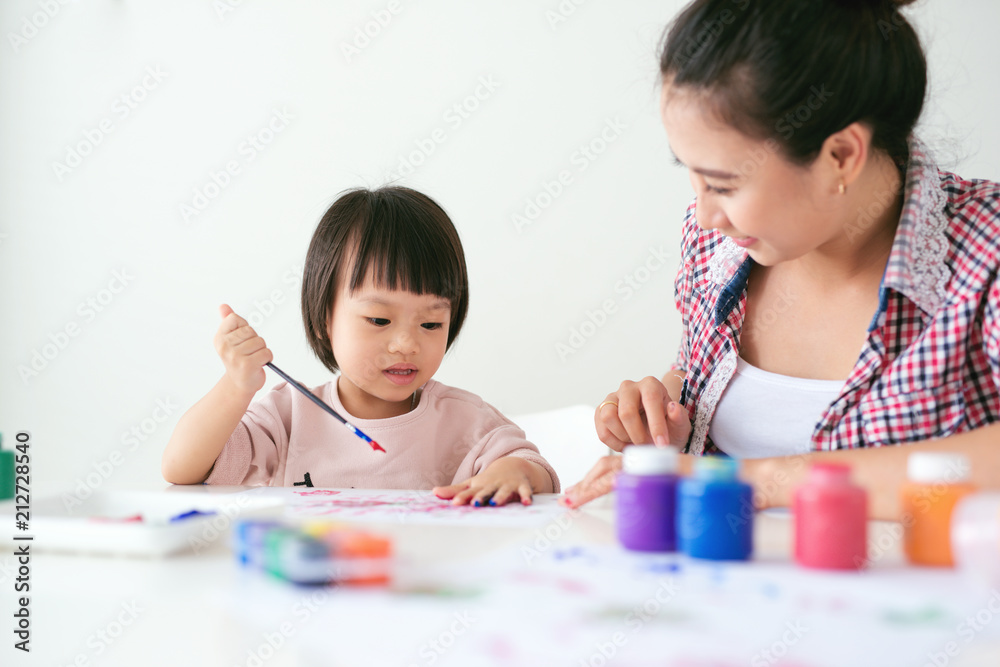 幸福的家庭，母亲和女儿一起画画。亚洲妇女帮助她的小女儿。