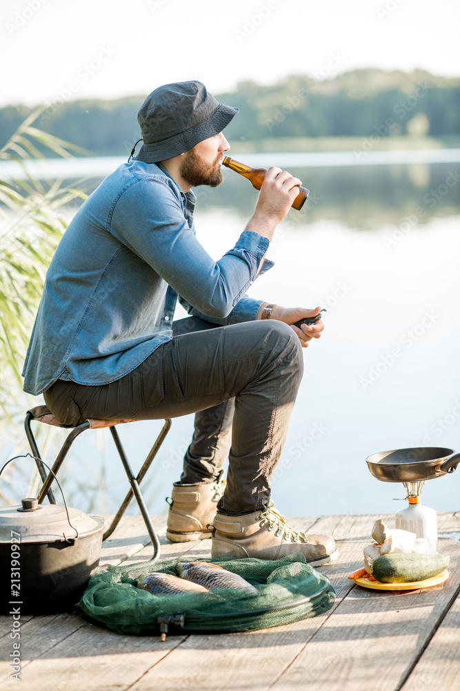 在湖边的码头上钓鱼的过程中，英俊的男人独自坐着喝啤酒放松