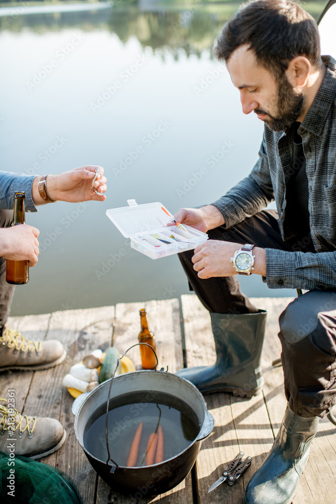 Two fishermen sitting together with fishing tackles sitting during the picnic near the lake