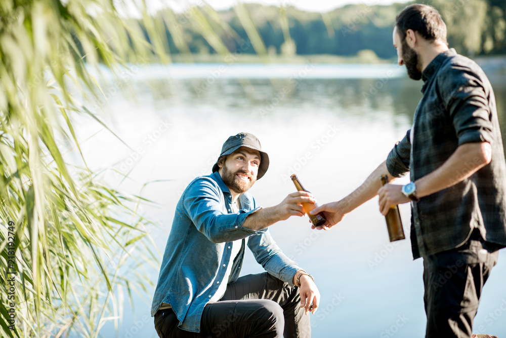 Two fishermen relaxing together with beer while fishing on the lake at the morning