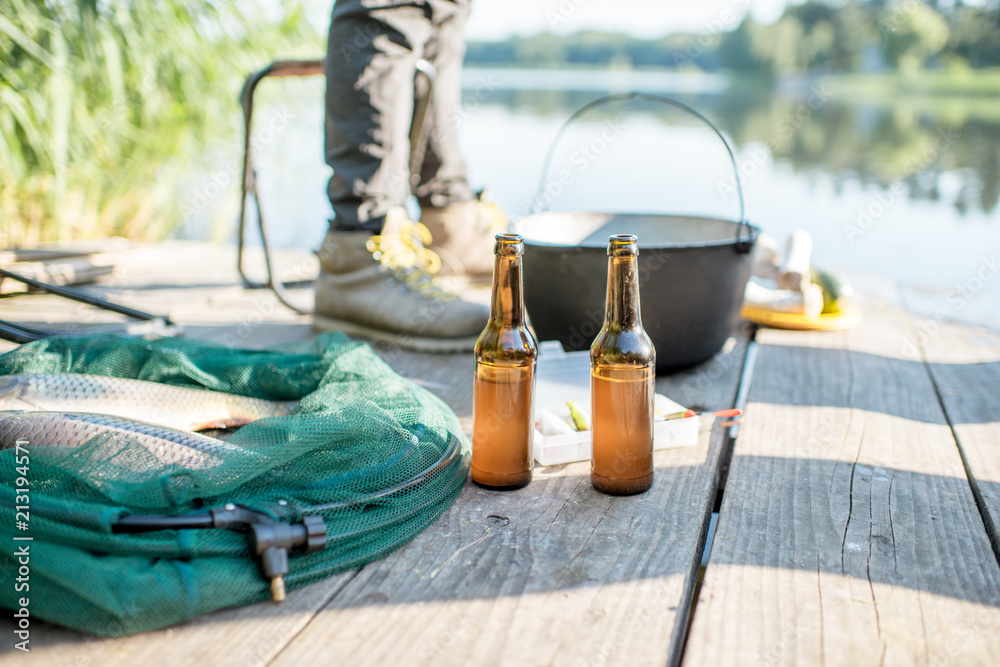 Wooden pier with fishing tackles and two bottles with beer near the lake