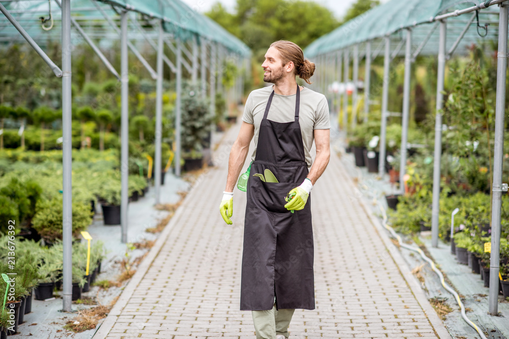 Handsome worker in uniform walking at the greenhouse with green plants for sale