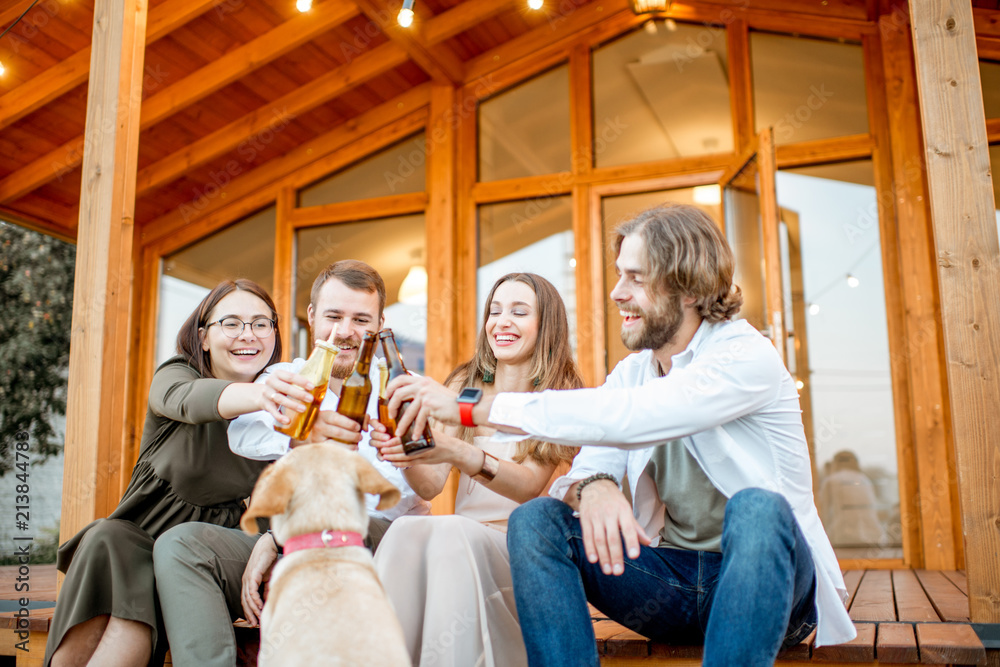 Young friends enjoying evening time sitting together with dog on the terrace of the modern wooden ho