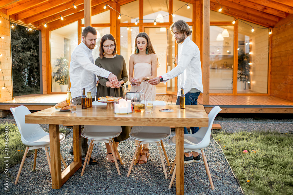 Four friends enjoying evening time having a dinner on the backyard of the modern country house outdo