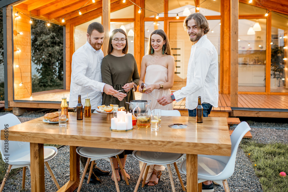 Four friends enjoying evening time having a dinner on the backyard of the modern country house outdo