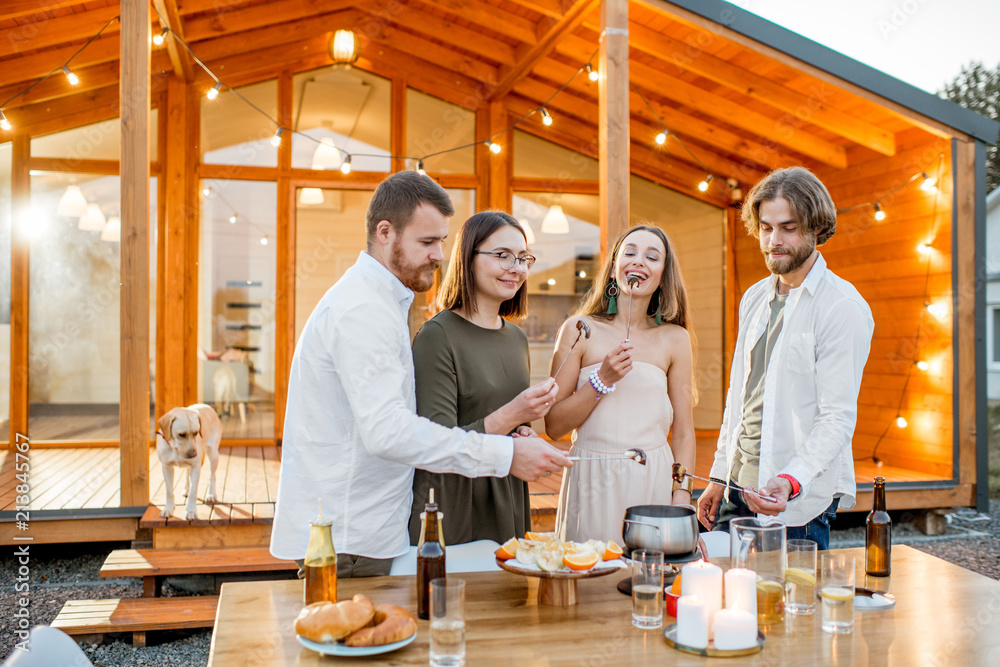 Four friends enjoying evening time having a dinner on the backyard of the modern country house outdo