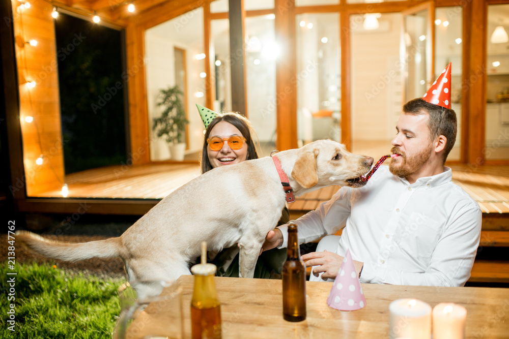 Funny dog with young couple sitting at the table during a celebration on the backyard of the house o