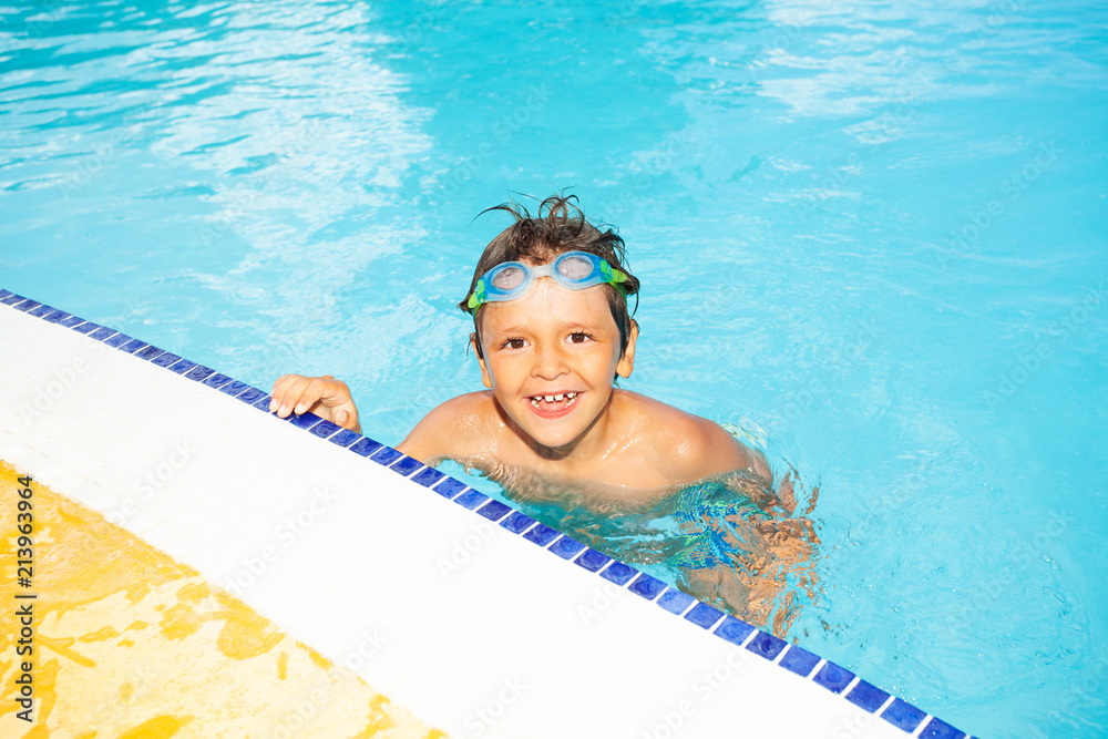 Happy boy resting at the edge of swimming pool