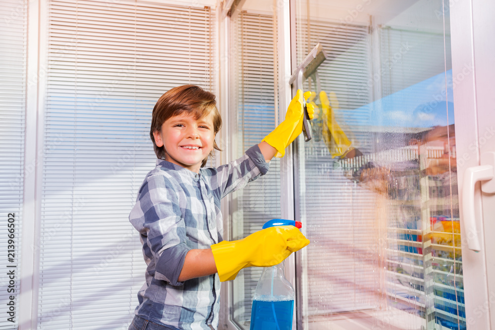 Smiling boy washing windows with window cleaner