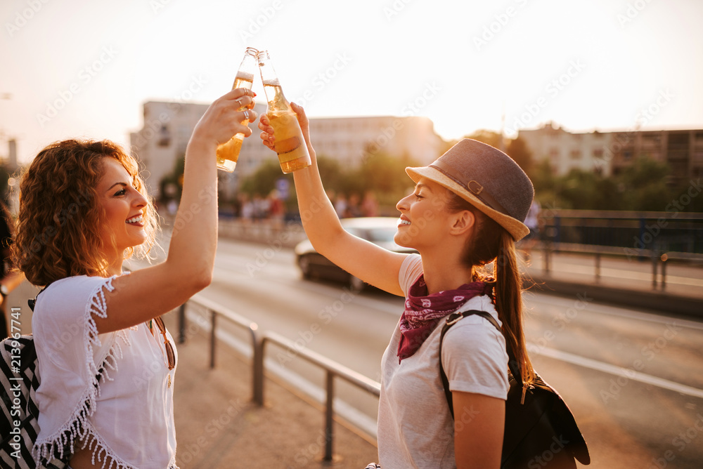 夏天，两个漂亮的时髦女孩在城市街道上敬酒。