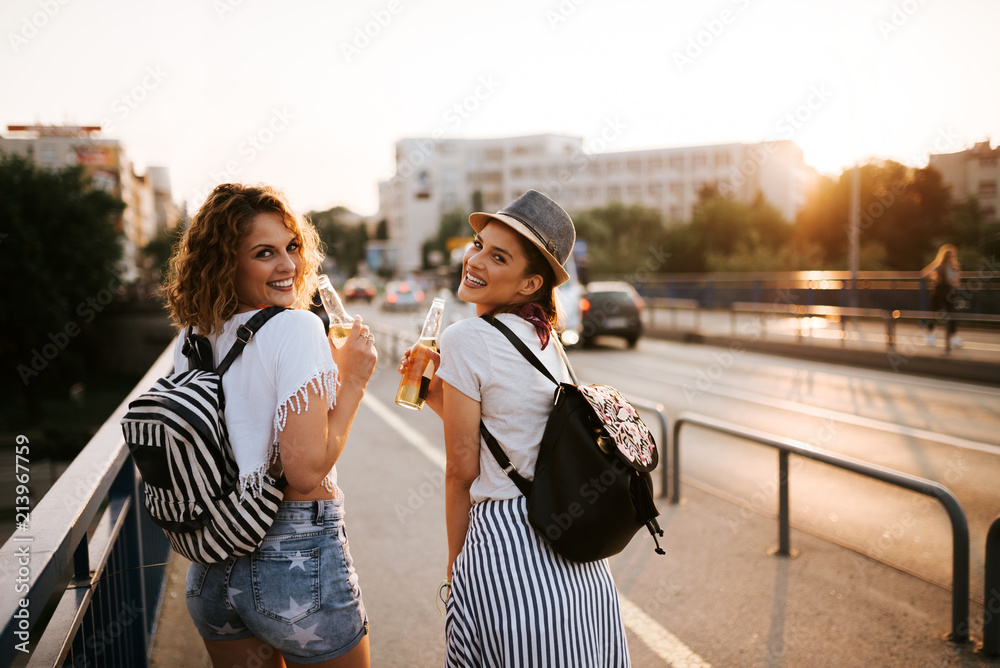 Two smiling festival party girls drinking while walking in the city.