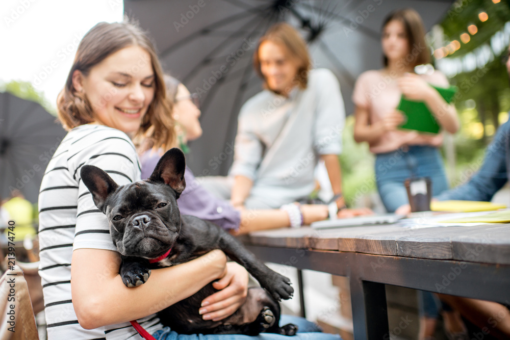 Young friends having fun together sitting with french bulldog during a studying outdoors in the park