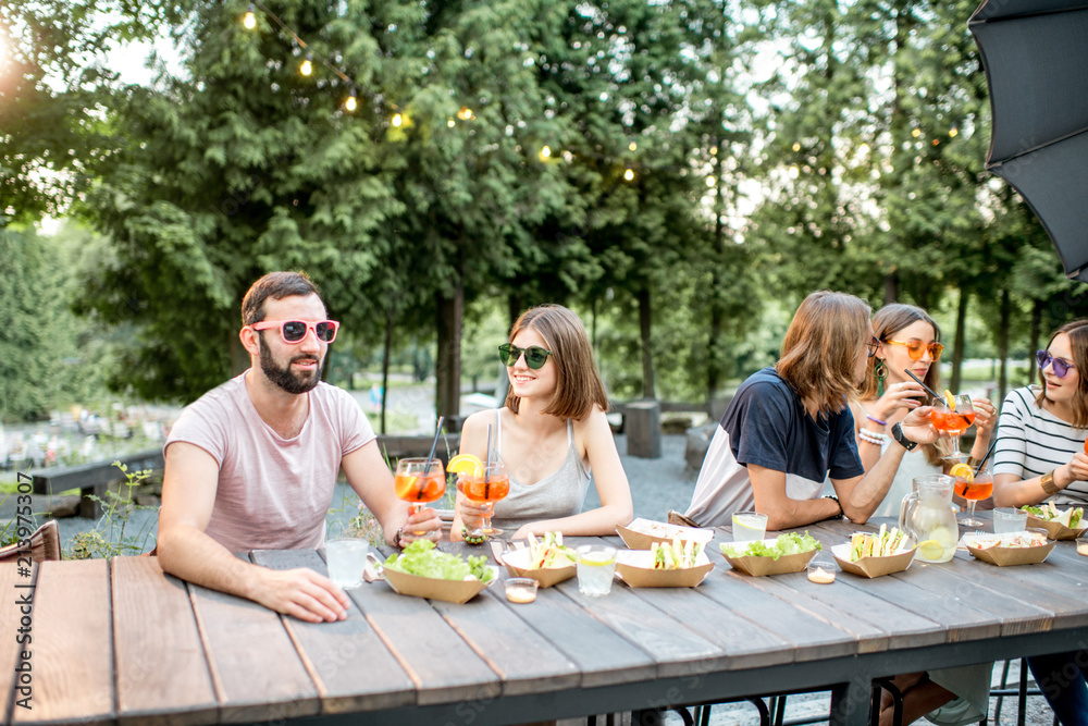 Young friends having fun together with snacks and drinks during the evening light outdoors in the pa