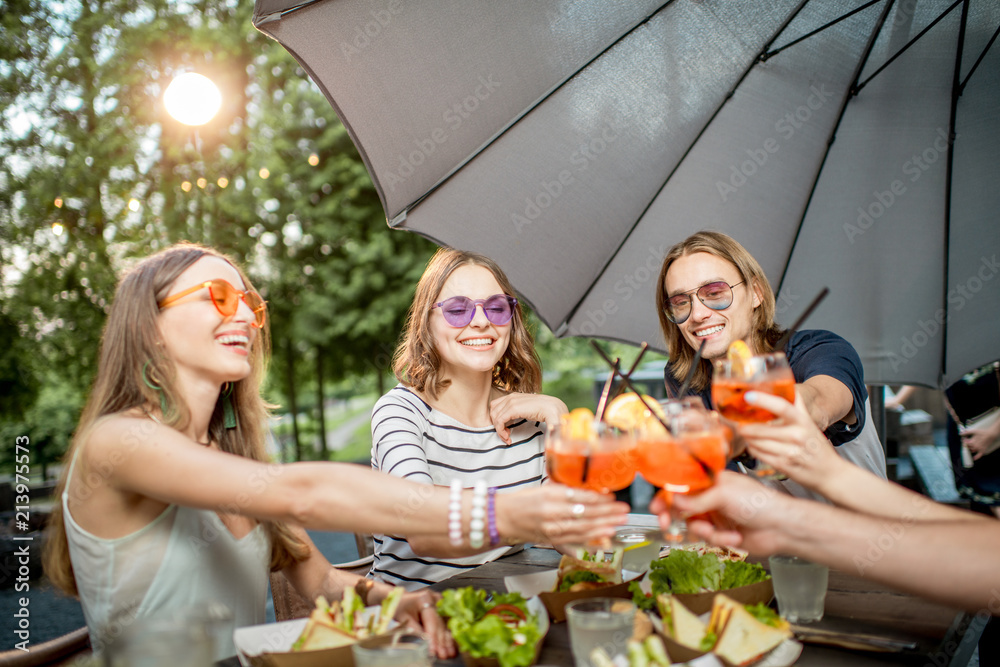 Young friends having fun together clinking glasses during the festive lunch outdoors in the park caf