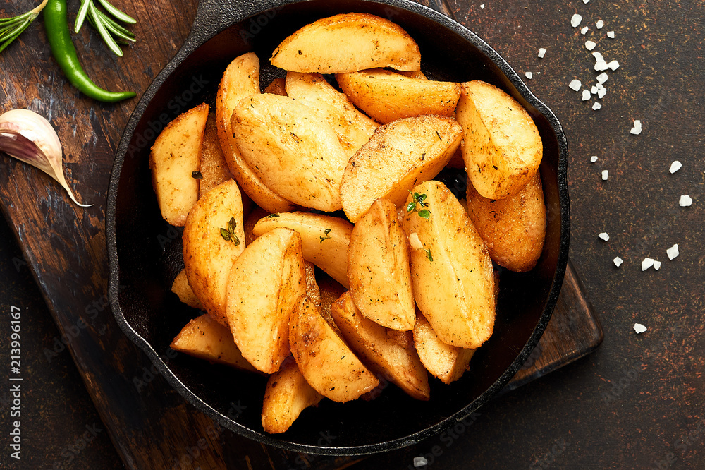 Fried potatoes in a pan on brown background