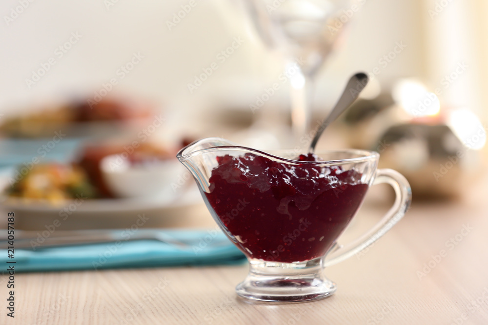 Gravy boat with tasty cranberry sauce on table