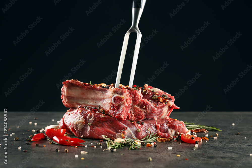 Composition with meat fork and raw steaks on table against black background