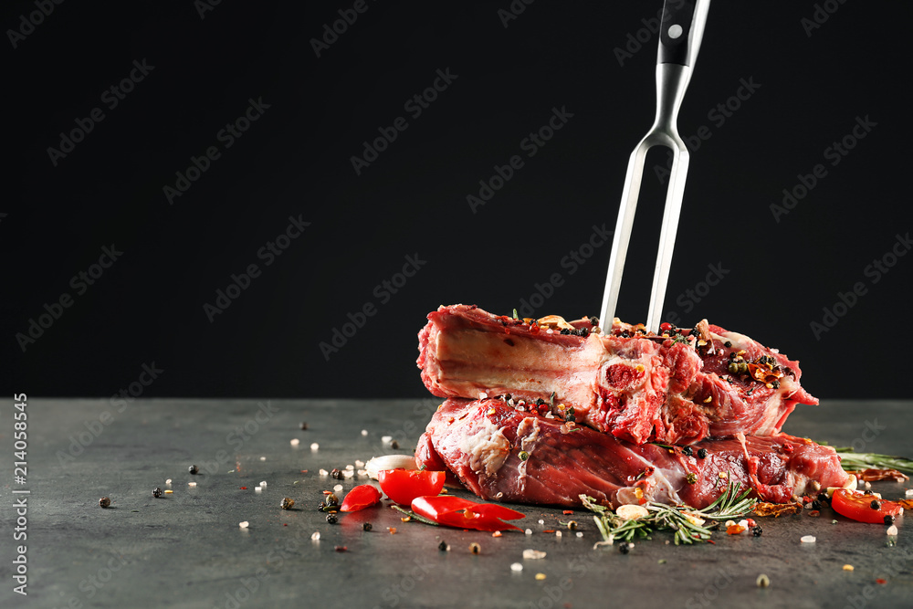 Composition with meat fork and raw steaks on table against black background