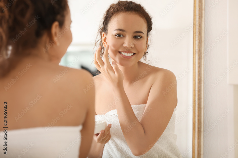 Morning of young African-American woman applying facial cream in bathroom