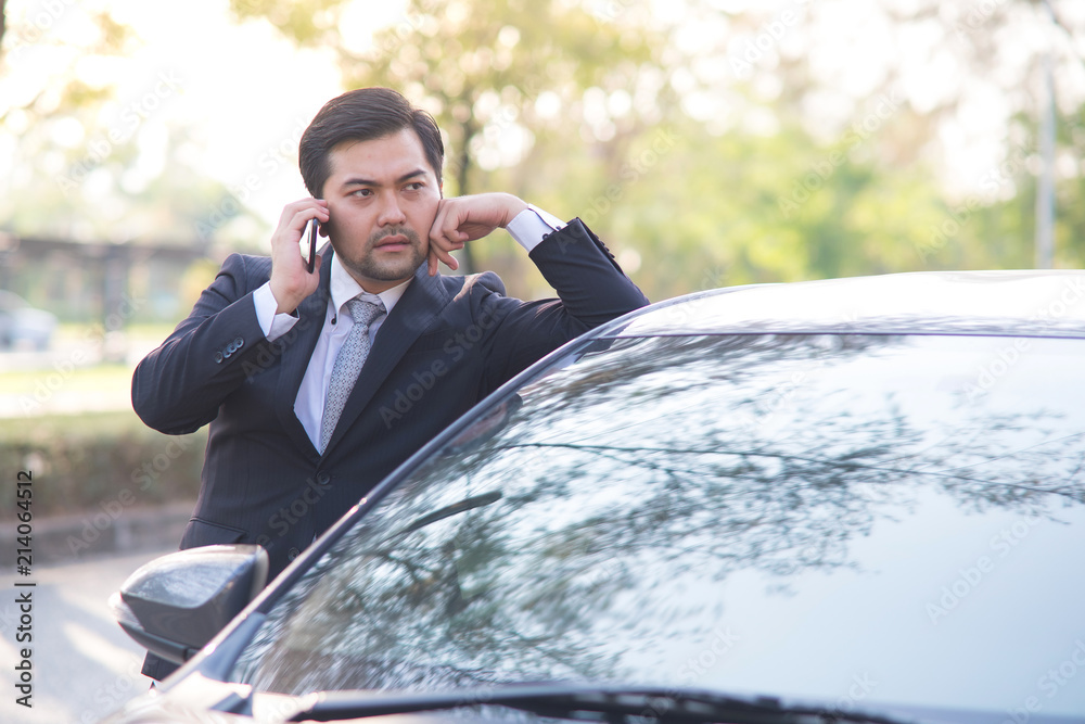 Handsome businessman using a mobile phone lerning on his car