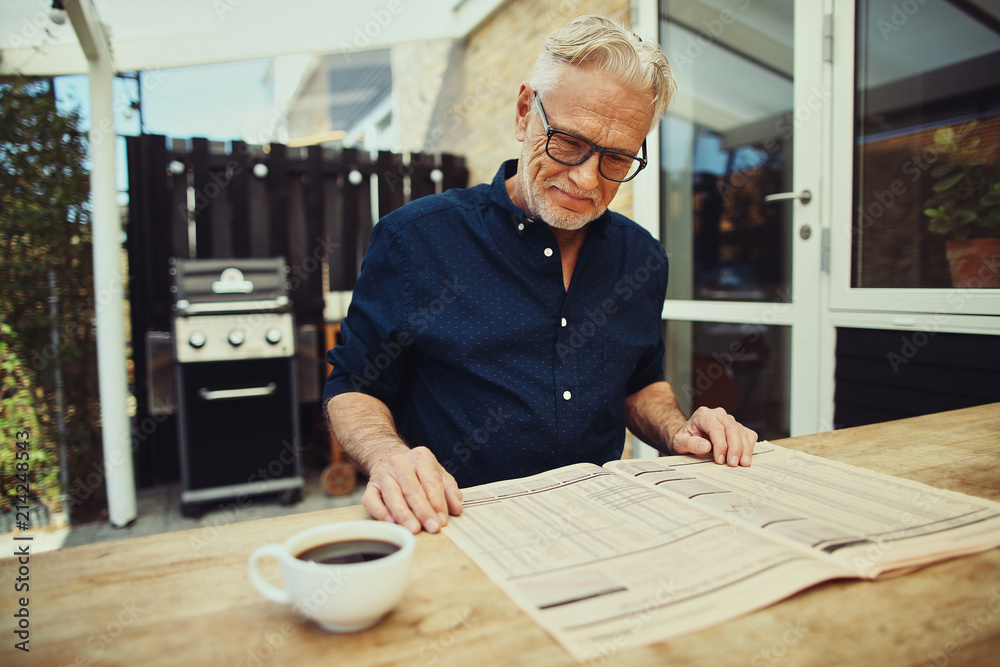 Smiling senior man enjoying a coffee and reading the newspaper