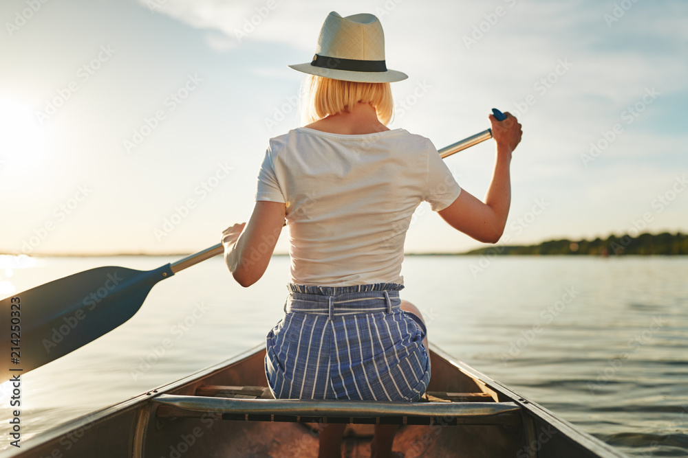 年轻女子夏天在平静的湖面上划独木舟