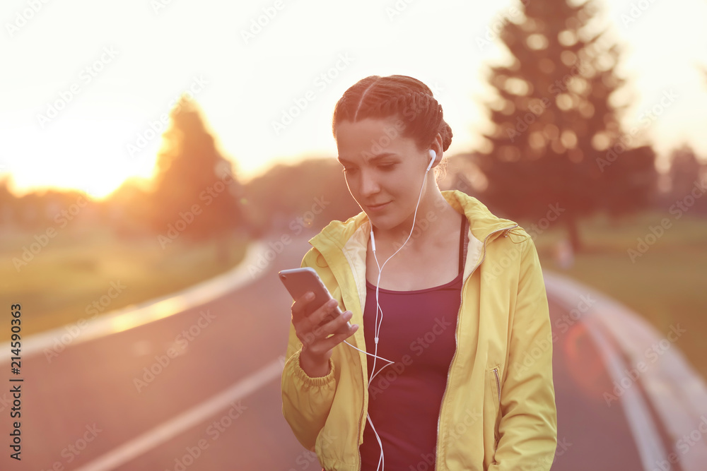 Sporty young woman with mobile phone listening to music outdoors in the morning