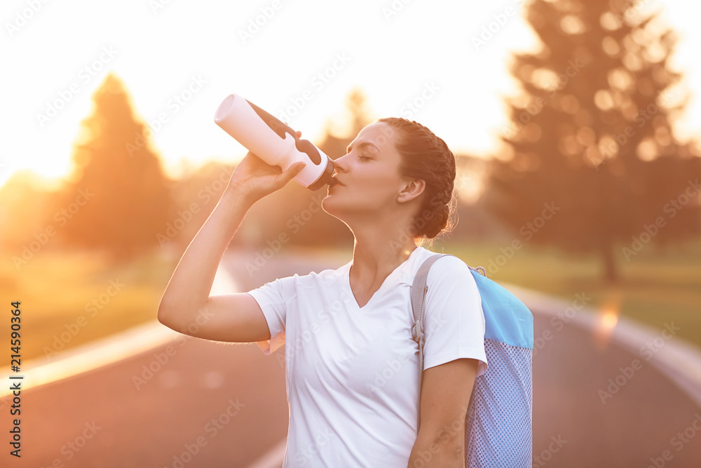 美丽的年轻女子早上在户外练习瑜伽后喝水