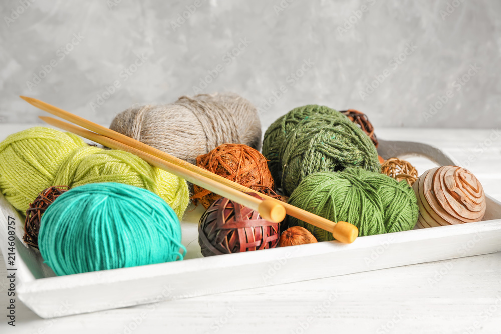 Tray with different knitting yarn and needles on table