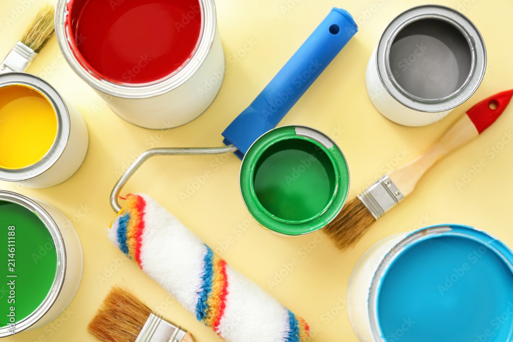 Paint cans with roller and brushes on color background