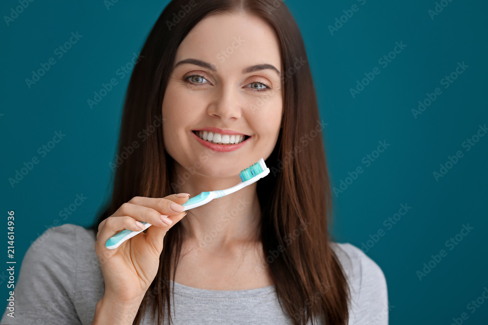 Young woman brushing her teeth on color background