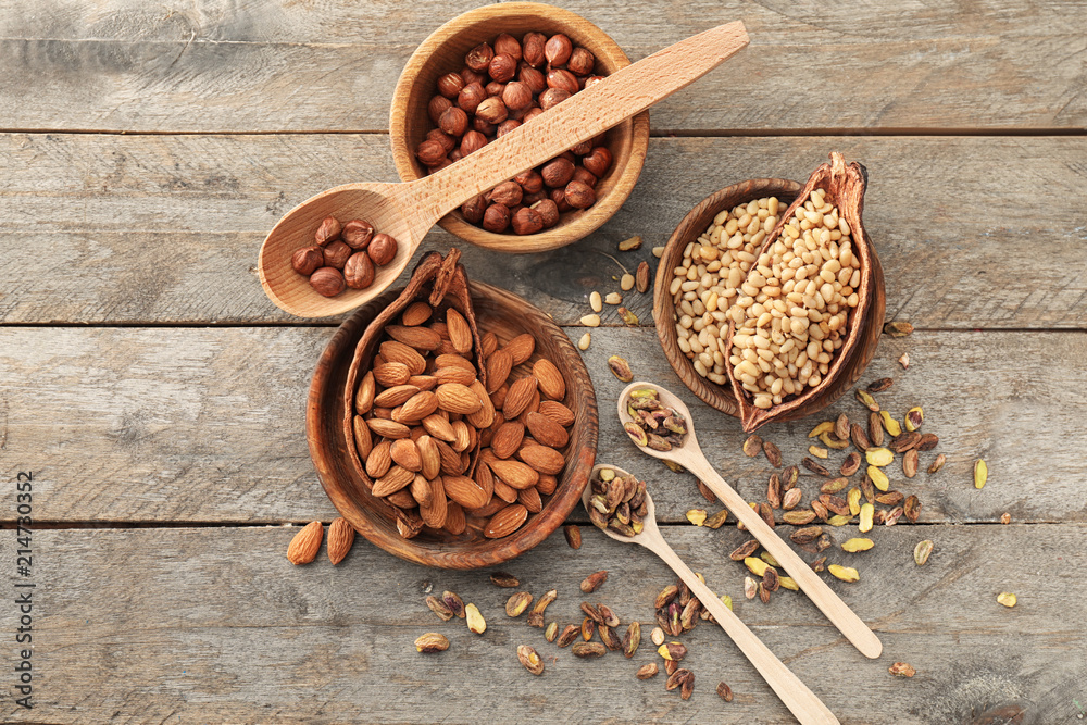 Bowls and spoons with different nuts on wooden background