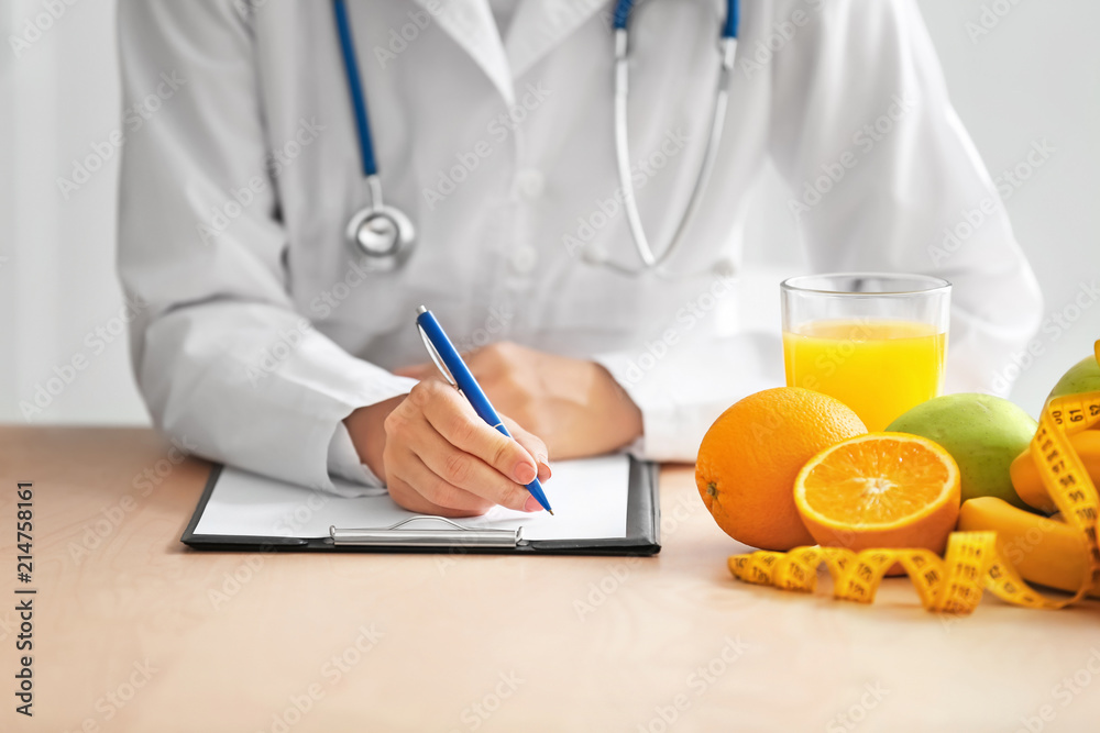 Female nutritionist sitting at table with fruits and clipboard in her office