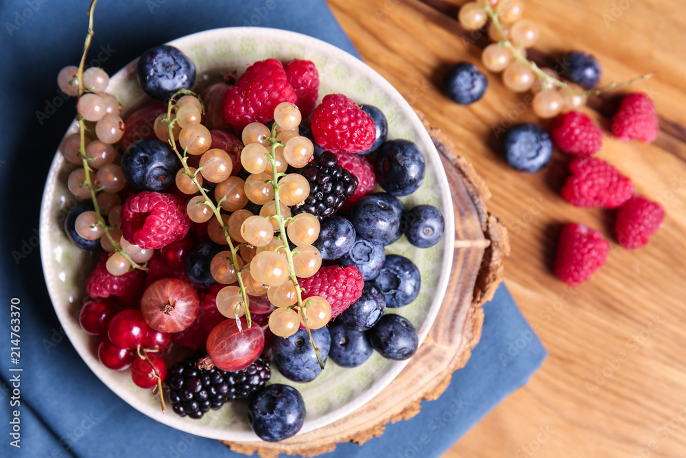 Plate with different ripe berries on wooden table