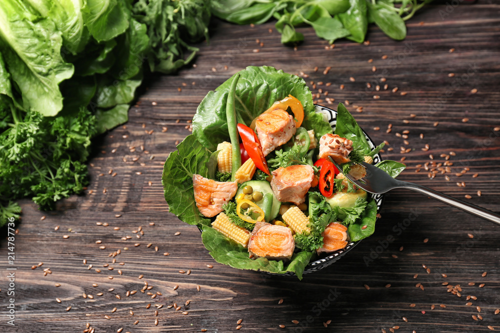 Tasty salad with fish and vegetables in bowl on wooden table