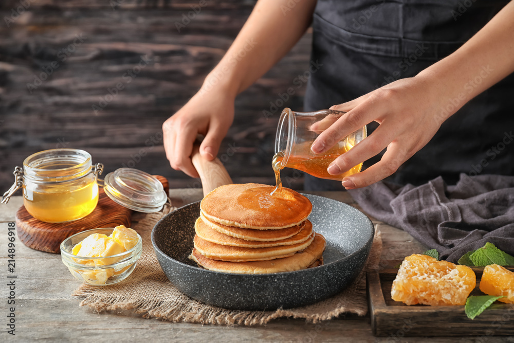 Woman pouring honey onto tasty pancakes at wooden table