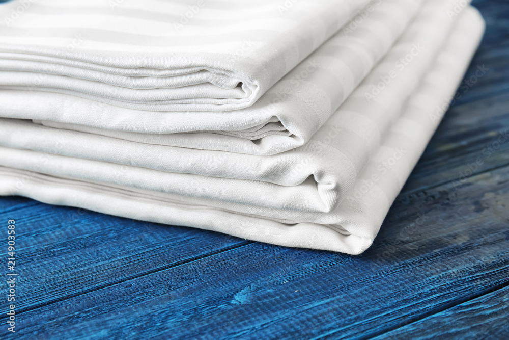 Stack of clean bed sheets on color wooden background, closeup