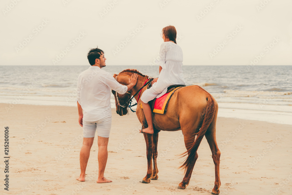 一对年轻夫妇在热带海滩上骑马。