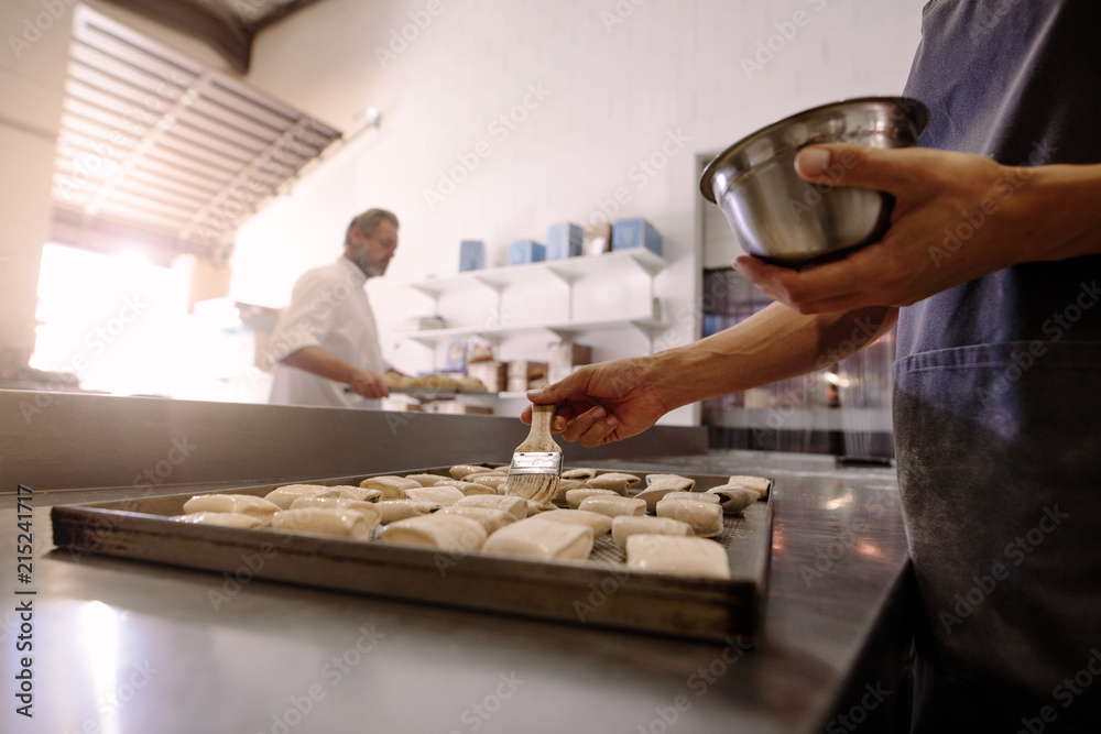 Baker with brush prepares rolls for baking