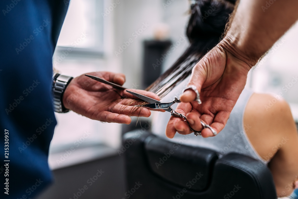 Close-up image of a male hairdresser cutting the hair of a female customer.