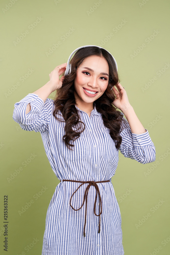 Beautiful young woman in headphone listening to music on green background