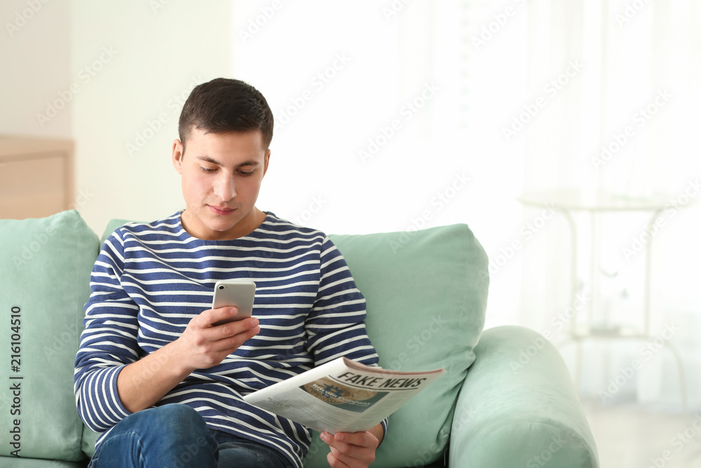 Handsome man with mobile phone and newspaper sitting on sofa at home